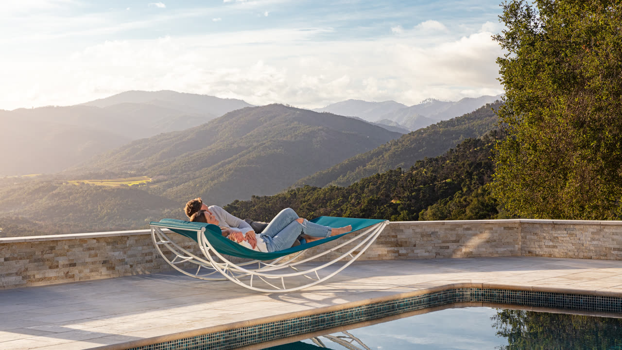 Two people resting on a Volo above a pool, looking out over the Carmel Valley in warm evening light