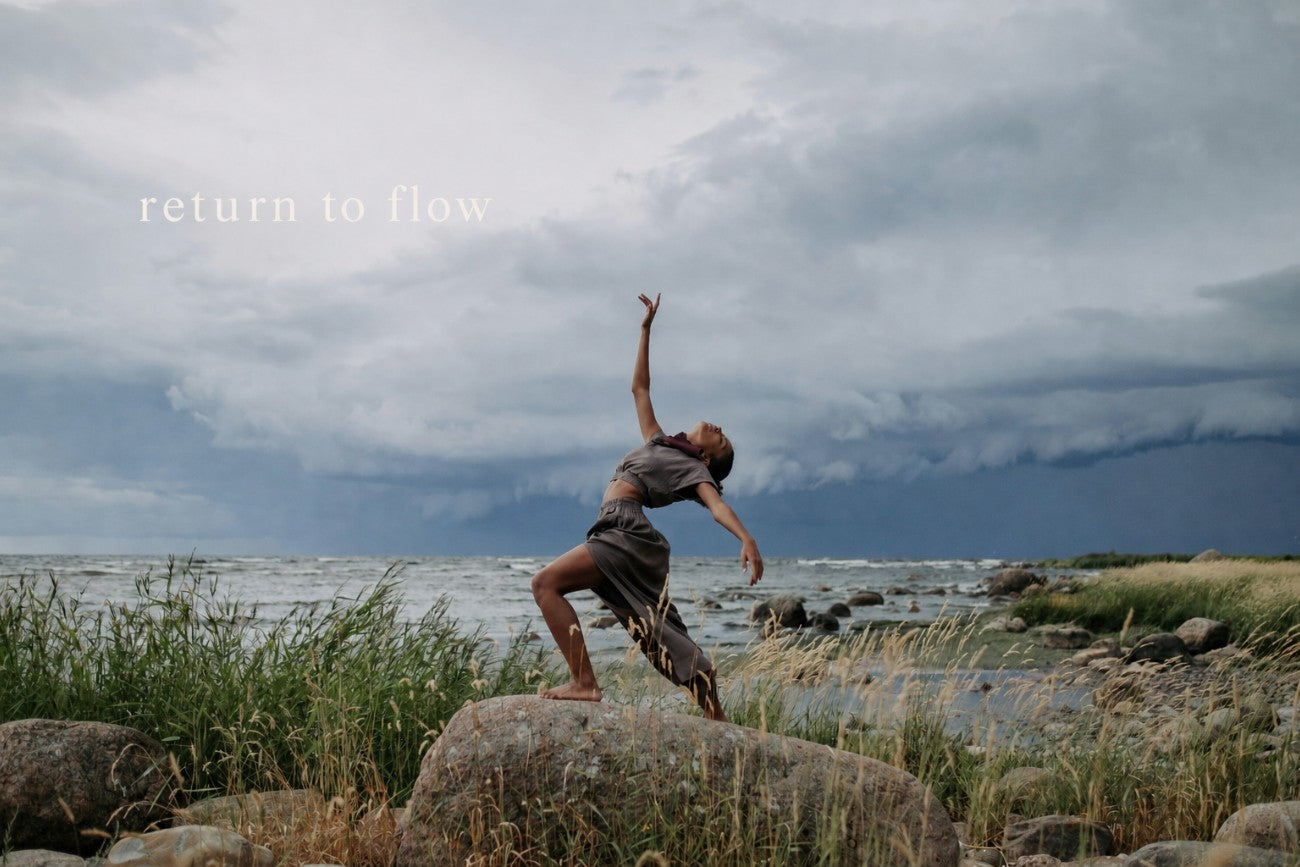A dancer mid-movement on rocks above the sea, under a storm sky