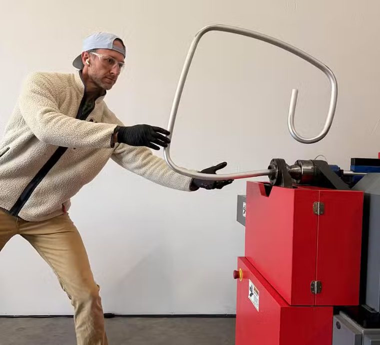 Jules Henry drawing a bent aluminium chair frame off the tube bender in the Bend workshop