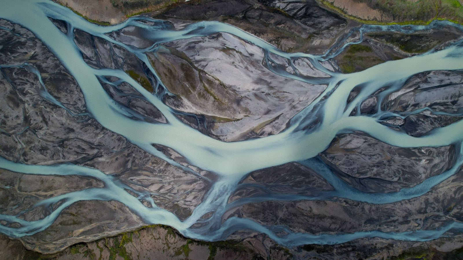 A braided glacial river seen from above, pale blue water through dark volcanic sand
