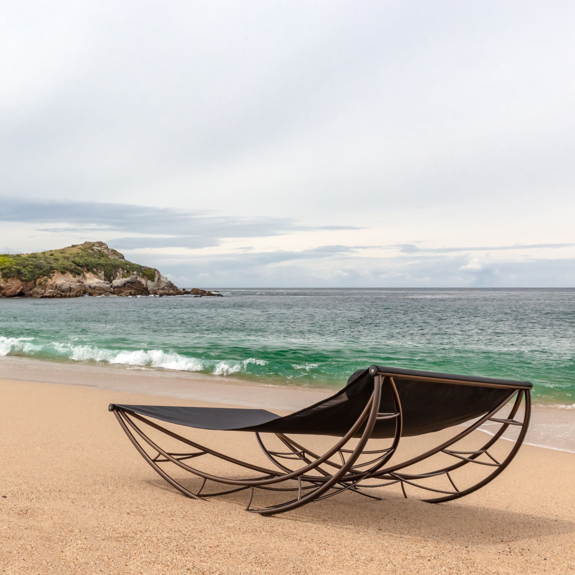 A Volo lounge with a black sling and bronze frame on a quiet beach